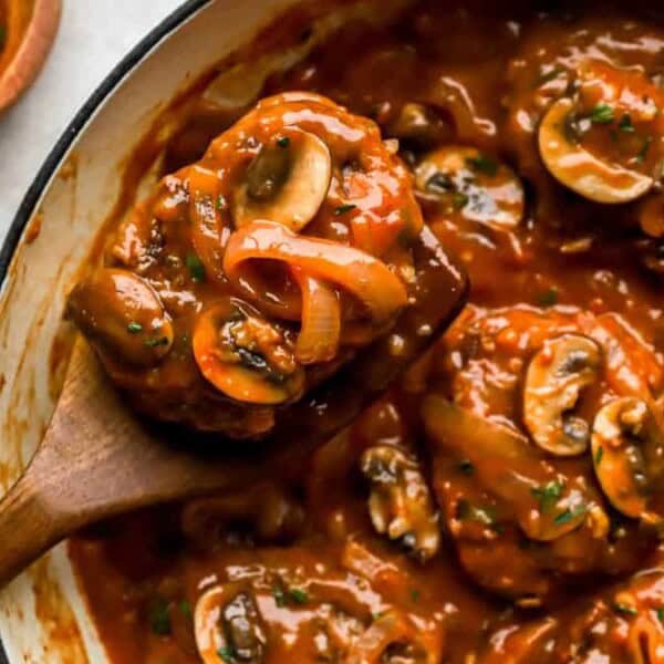 Chicken, ground beef, and sliced mushrooms in tomato-based sauce inside a white pot with a wooden spoon.