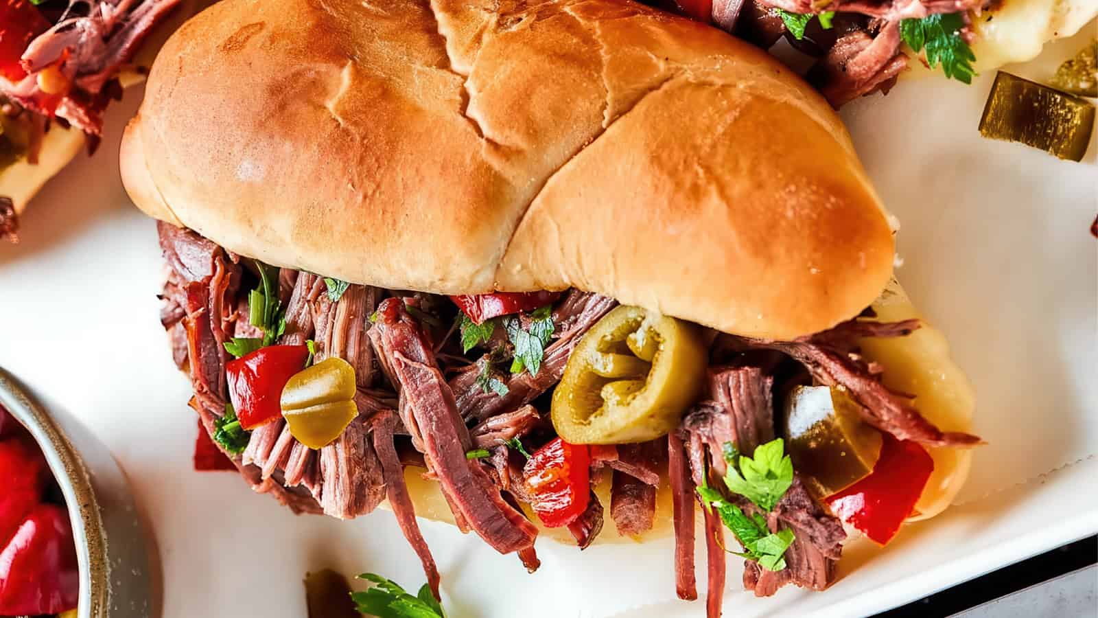A juicy sandwich filled with shredded beef, sliced jalapeños, red bell peppers, and garnished with fresh parsley, served on a soft bun. Served with