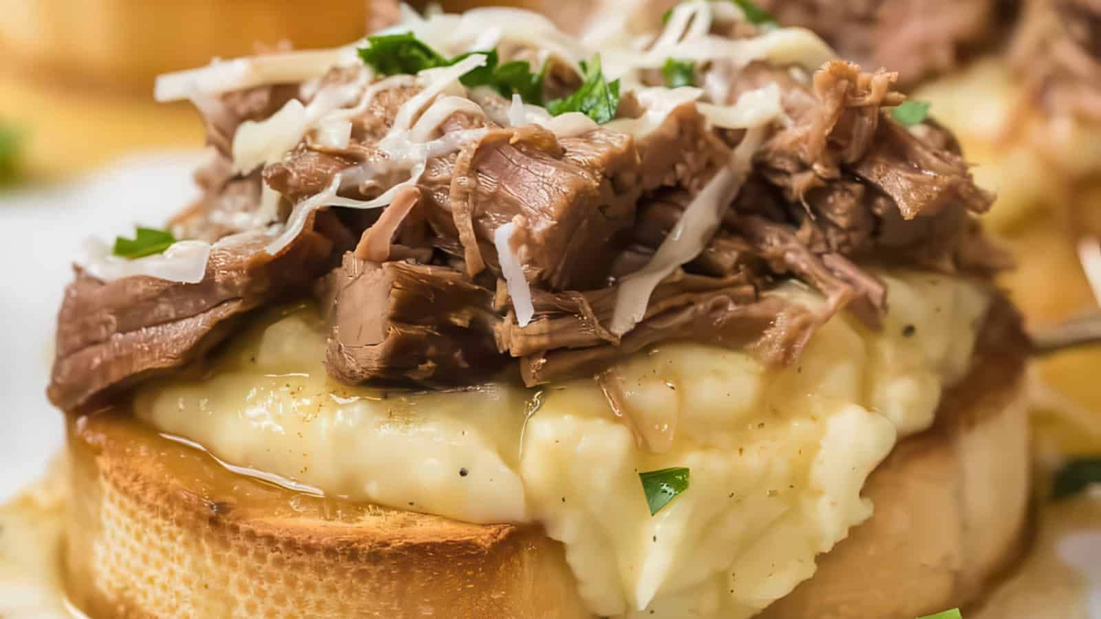 Close-up of an open-faced sandwich with layers of tender shredded meat on top of creamy mashed potatoes, garnished with grated cheese and chopped herbs, all resting on a slice of toasted bread.
