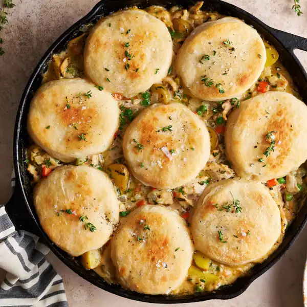 A skillet filled with chicken stew and individual savory biscuits.