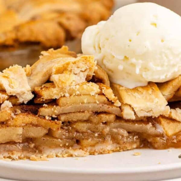 A slice of apple pie topped with a scoop of vanilla ice cream, served on a white plate with a fork beside it.