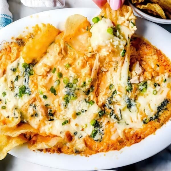 A dish of cheesy buffalo chicken dip topped with melted cheese and green onions, served on a white oval platter. Chips are partially visible around the dish, suggesting it is being used for dipping.
