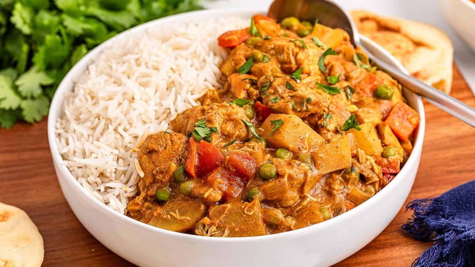 A bowl of creamy chicken curry with vegetables served over fluffy white rice, garnished with fresh herbs, alongside naan bread.