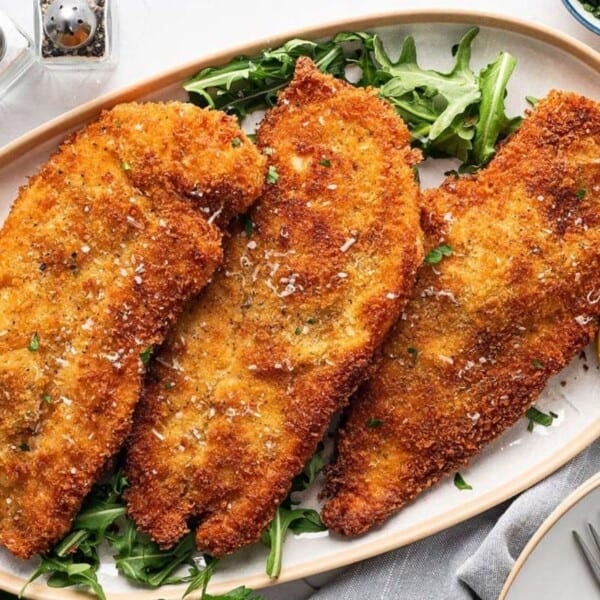 Three fish fillets served with lemon wedges and sprinkled with parsley, arranged on a plate.