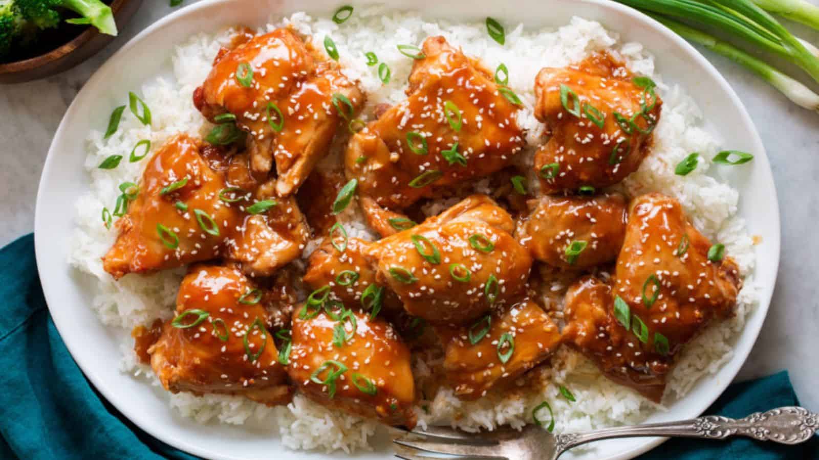 Tender chicken thighs glazed in a shiny sauce, served over a bed of fluffy white rice, garnished with sliced green onions and sesame seeds.