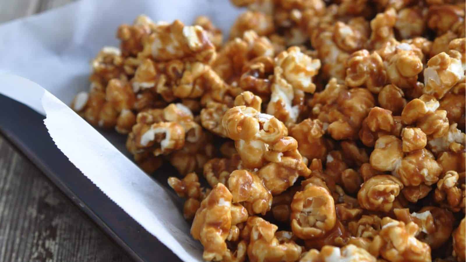 Caramel-coated popcorn piled on parchment paper, glistening with a sweet sheen and inviting texture, perfect for snacking.