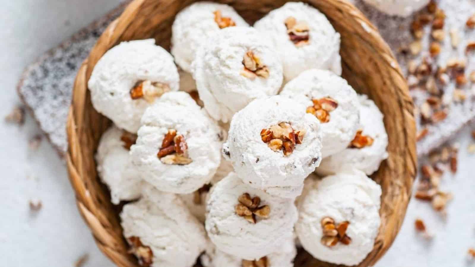 A woven basket filled with white, fluffy dessert balls topped with chopped pecans, resting on a light surface with scattered nuts.