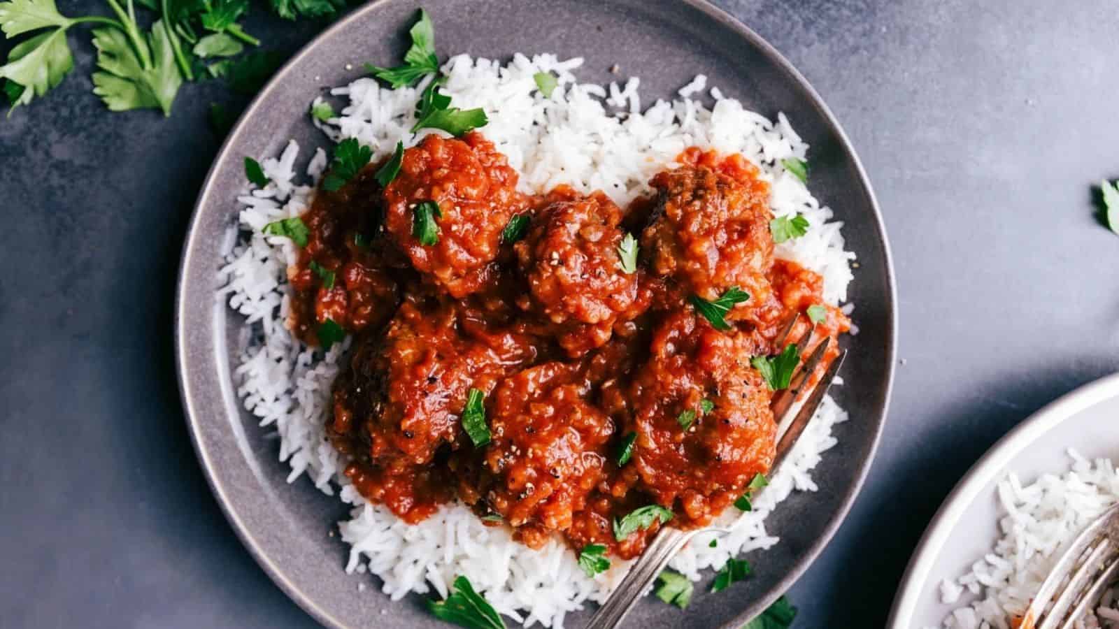 A plate of meatballs in rich tomato sauce served over fluffy white rice, garnished with fresh parsley for color and flavor.