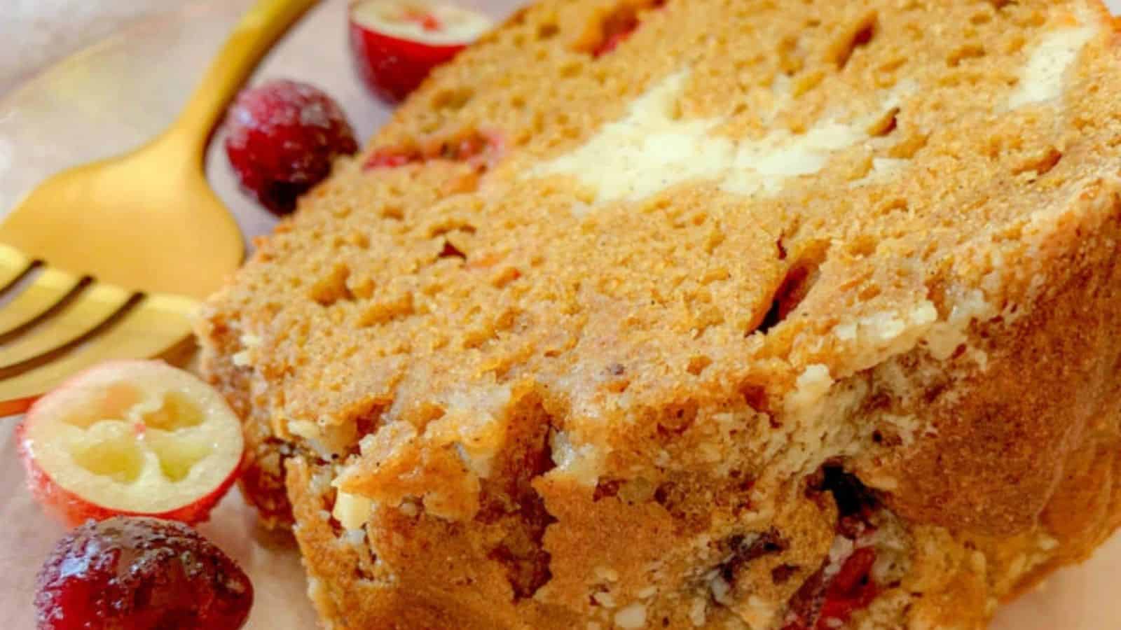 A slice of golden-brown cranberry bread, garnished with fresh cranberries, and a golden fork nearby, resting on a delicate plate.