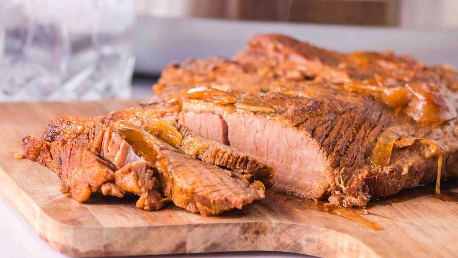 Sliced, juicy roast beef on a wooden cutting board, with a glass of ice in the background, showcasing a golden glaze.