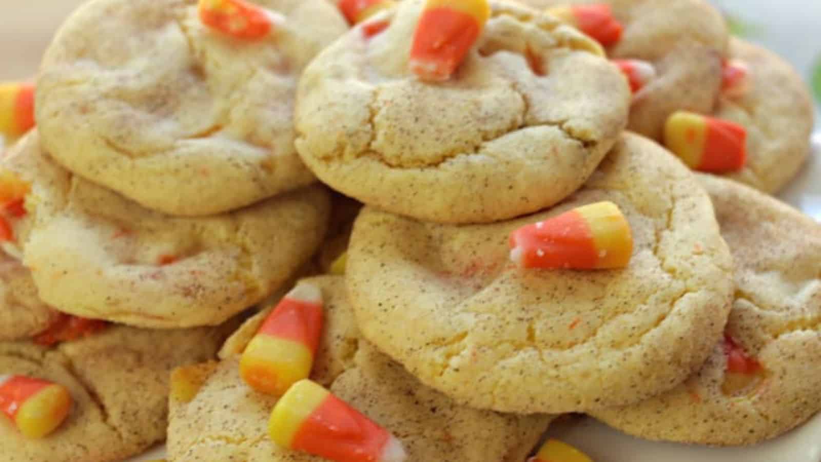 A stack of soft, golden cookies topped with colorful candy corn, featuring a sprinkle of cinnamon on a white plate