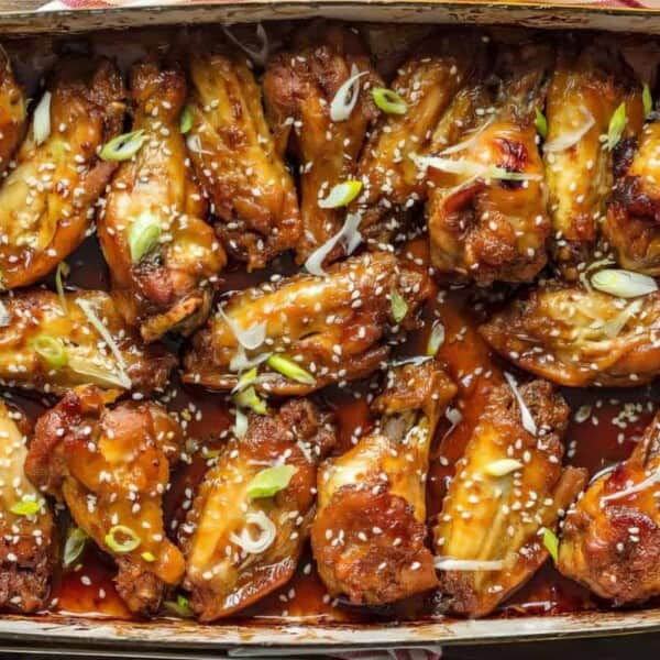 A rectangular baking dish filled with chicken wings, garnished with slices of green onion and sesame seeds.