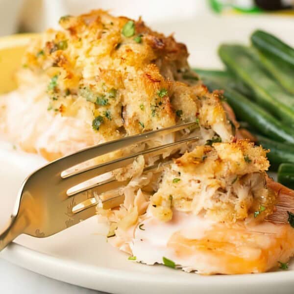 A fork cutting into a stuffed salmon fillet with herbs, accompanied by green beans and a lemon wedge on a plate.