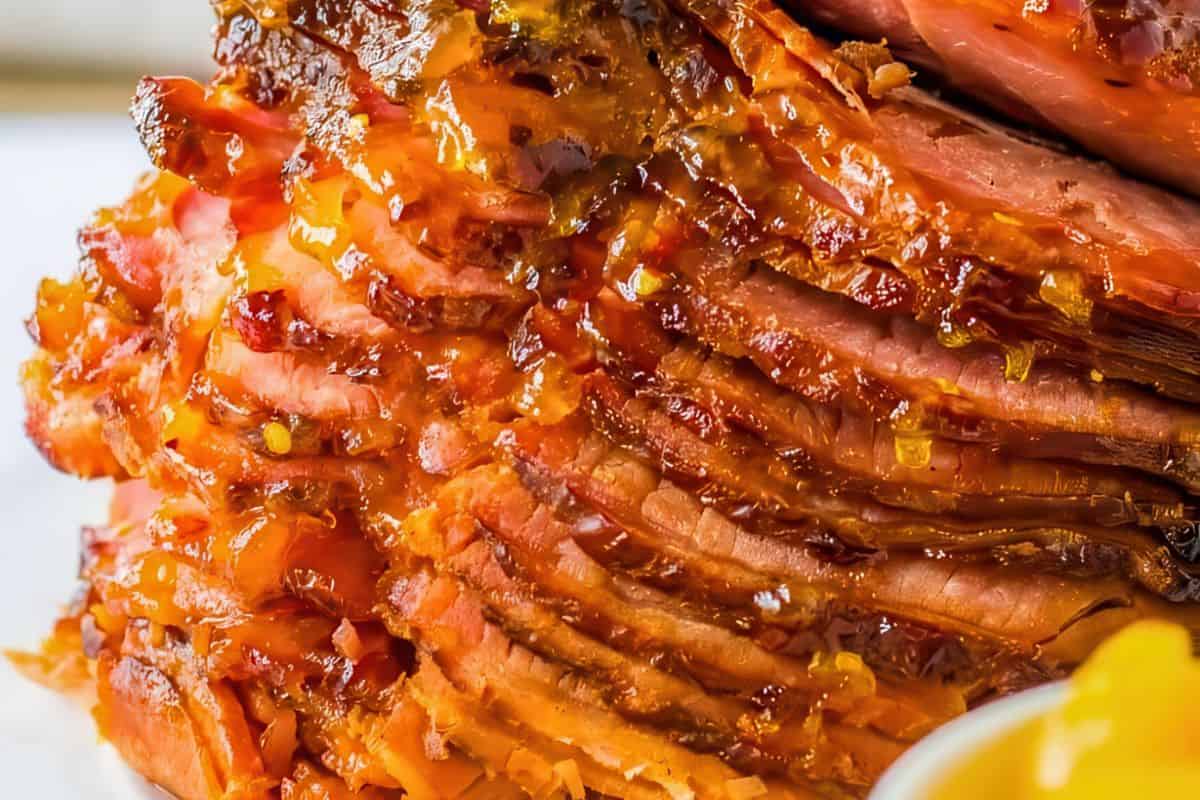 Close-up of sliced glazed ham, showing layers of juicy, caramelized meat with a shiny, golden-brown coating.