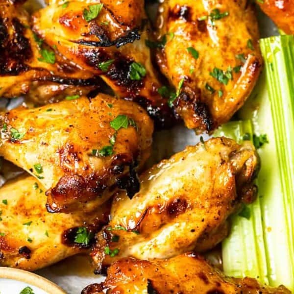 The image shows grilled chicken wings garnished with herbs, accompanied by celery sticks and a small bowl of dipping sauce.