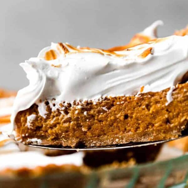 A slice of pumpkin pie with whipped topping is in a glass pie dish.