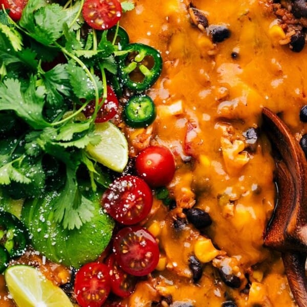 The image features a skillet containing cheesy Mexican rice, black beans, corn, cherry tomatoes, jalapeño slices, with lime wedges and cilantro as garnish.