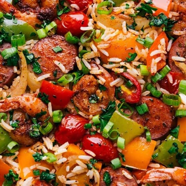The image shows rice, shrimp, sliced sausage, bell peppers, tomatoes, green onions, and chopped herbs.