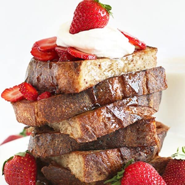 The image features a stack of French toast topped with strawberries and whipped cream, accompanied by a glass of milk in the background.