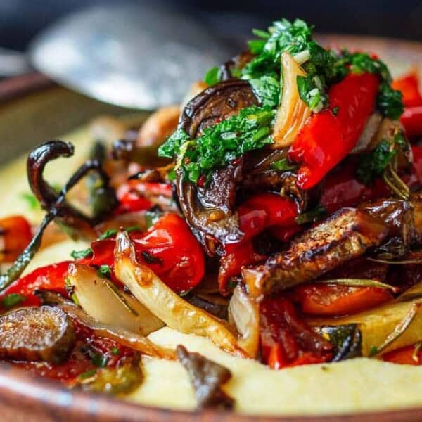 A bowl of polenta topped with roasted eggplant, zucchini, and bell peppers, garnished with fresh herbs.