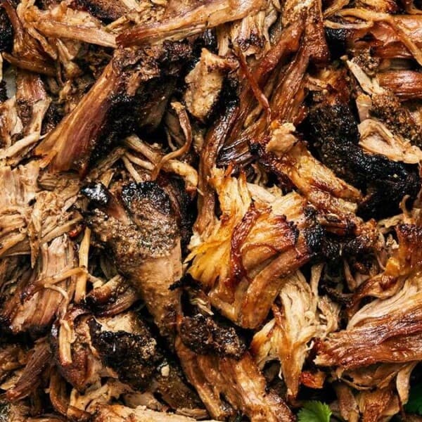 Shredded cooked meat with charred edges, lime wedges, and cilantro on a plate.