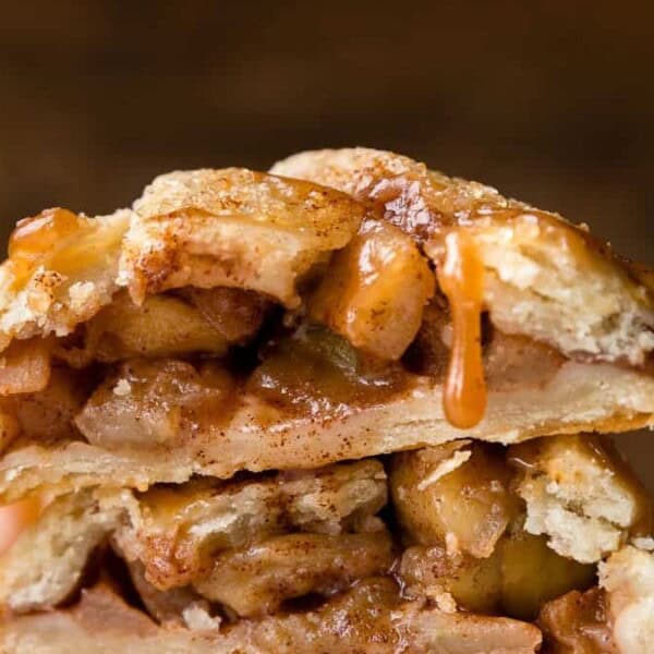 The image shows two stacked slices of apple pie with a flaky crust, filled with spiced apple chunks and drizzled with caramel sauce.