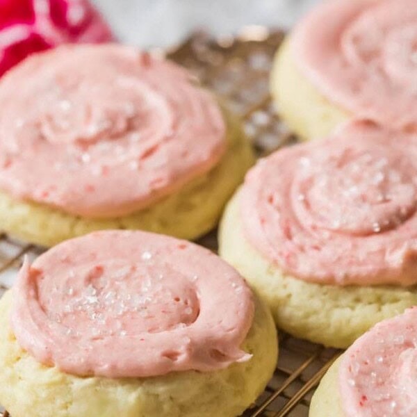 Six cookies with pink frosting and colorful sprinkles on a cooling rack.
