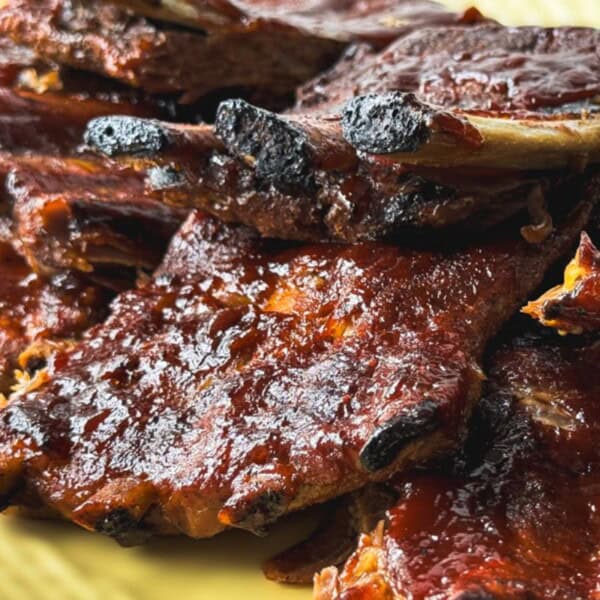 A close-up of a stack of barbecued ribs with a glazed, caramelized surface on a yellow plate.