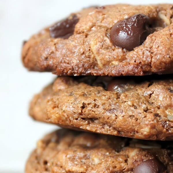 Close-up of a stack of chocolate chip cookies. The cookies are thick, with visible chocolate chips embedded in them, showcasing a golden-brown, crumbly texture against a neutral background.