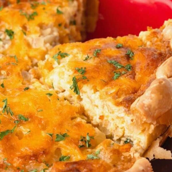 Close-up of a cheesy baked quiche topped with parsley, with a slice cut out, displayed in a red dish.