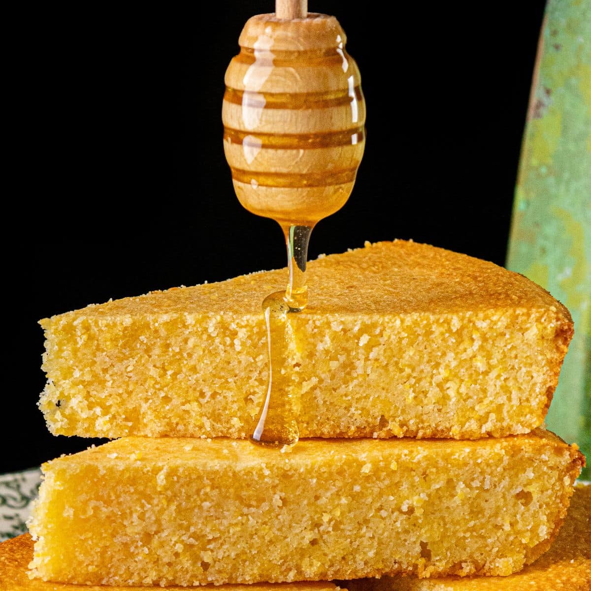Two slices of cornbread stacked with honey being drizzled from a dipper above.