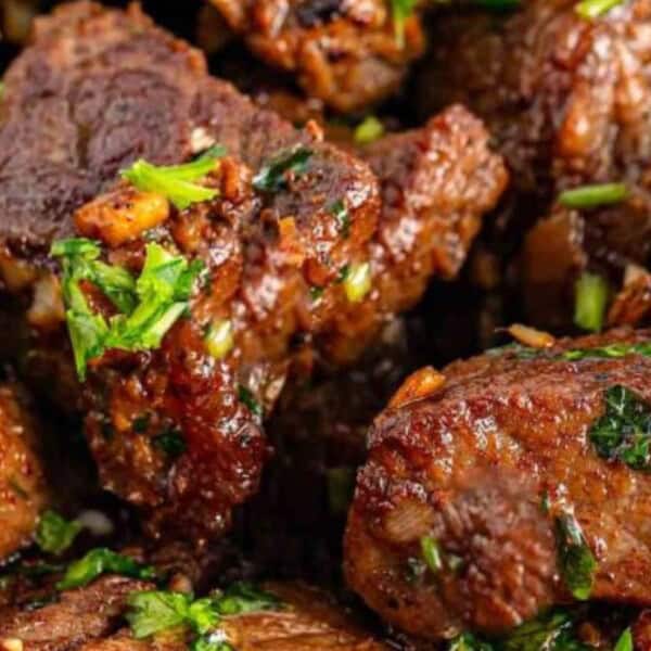 Succulent pieces of beef, garnished with fresh green herbs and spices, creating a mouthwatering, flavorful dish.