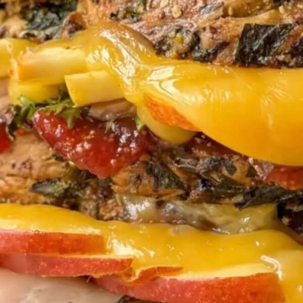 A close-up of a gourmet sandwich featuring layers of vibrant cheeses, deli meats, and fresh apple slices on multigrain bread.