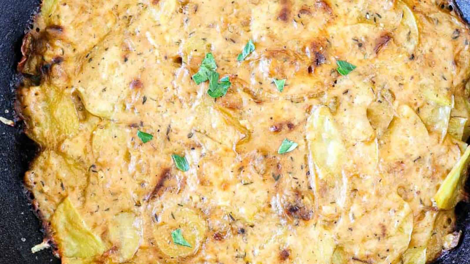 A golden-brown, baked dish featuring layered potato slices, herbs, and a creamy sauce, garnished with fresh green leaves.