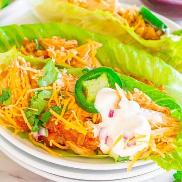 Lettuce wraps filled with shredded chicken, cheese, and green peppers, garnished with cilantro and sour cream on a white plate.
