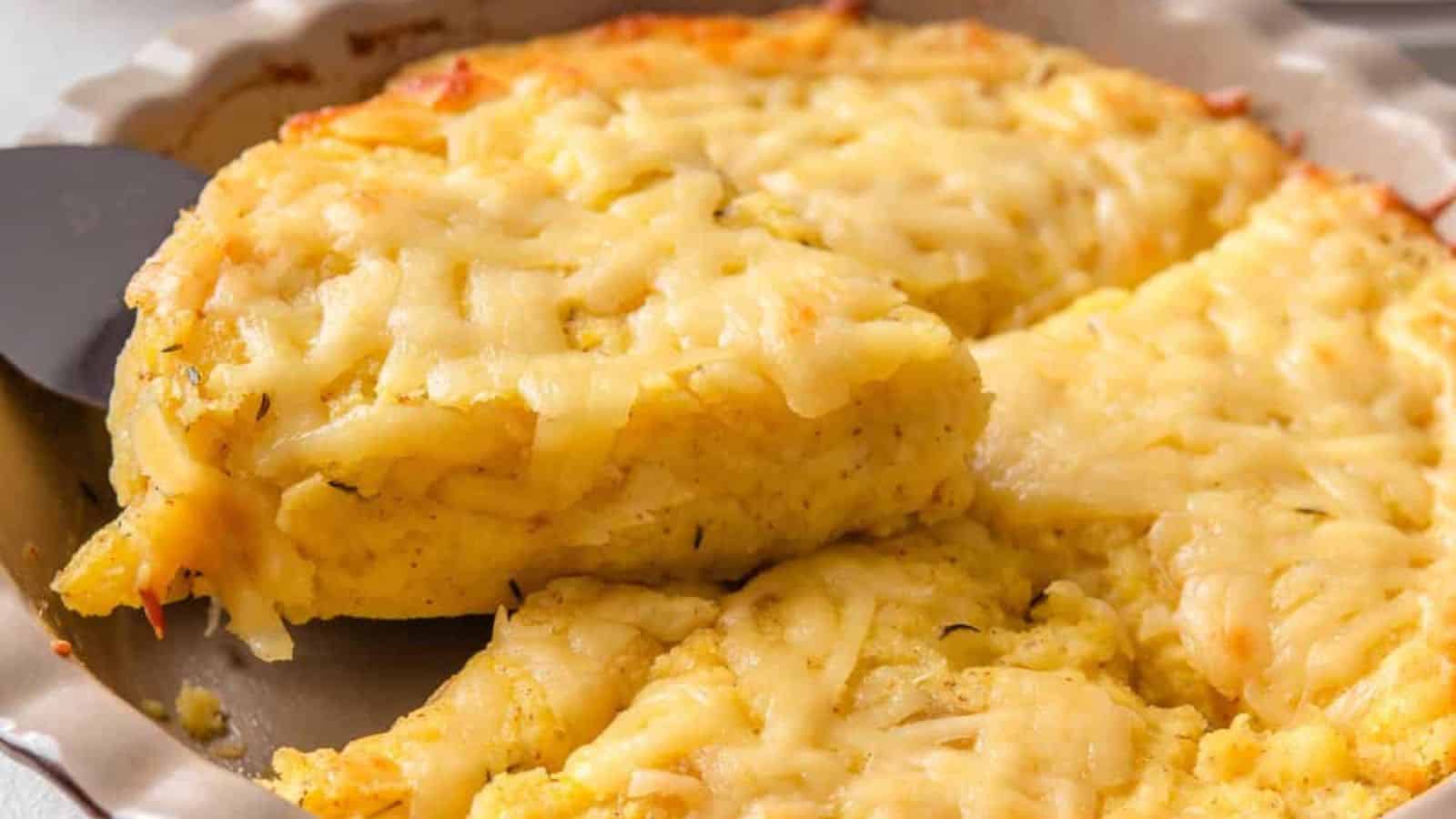 A close-up of a golden, cheesy baked dish with a slice removed, showcasing a creamy texture and a crispy top in a round pan.