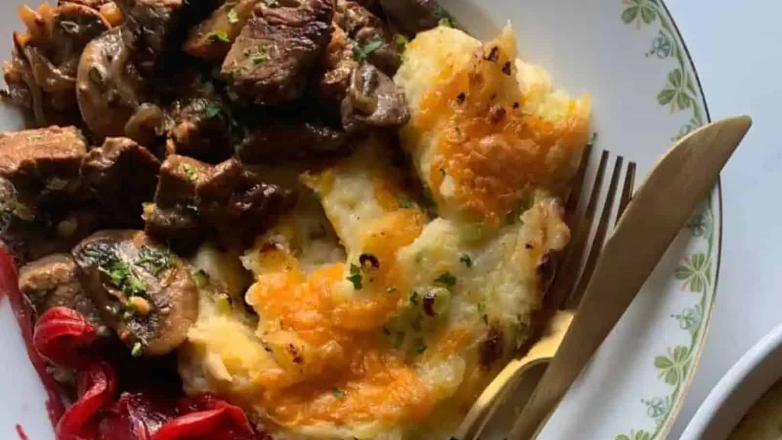 A hearty plate featuring tender beef chunks, sautéed mushrooms, cheesy mashed potatoes, and vibrant red peppers, garnished with herbs.