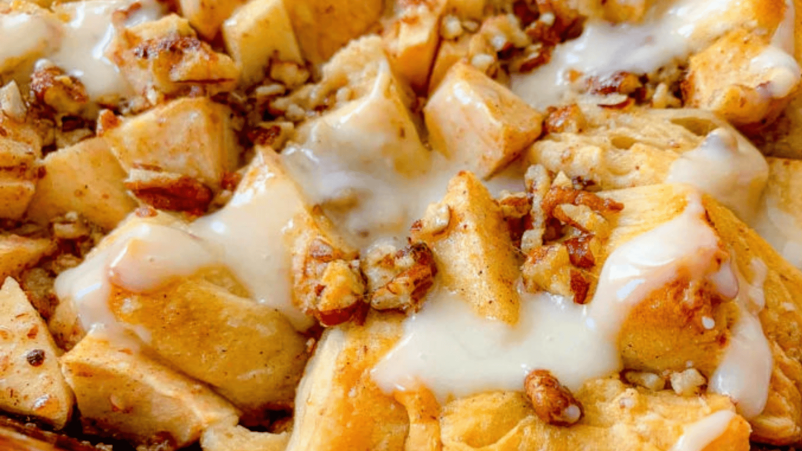 Cinnamon apple bread pudding topped with cream and chopped pecans, served warm in a baking dish.