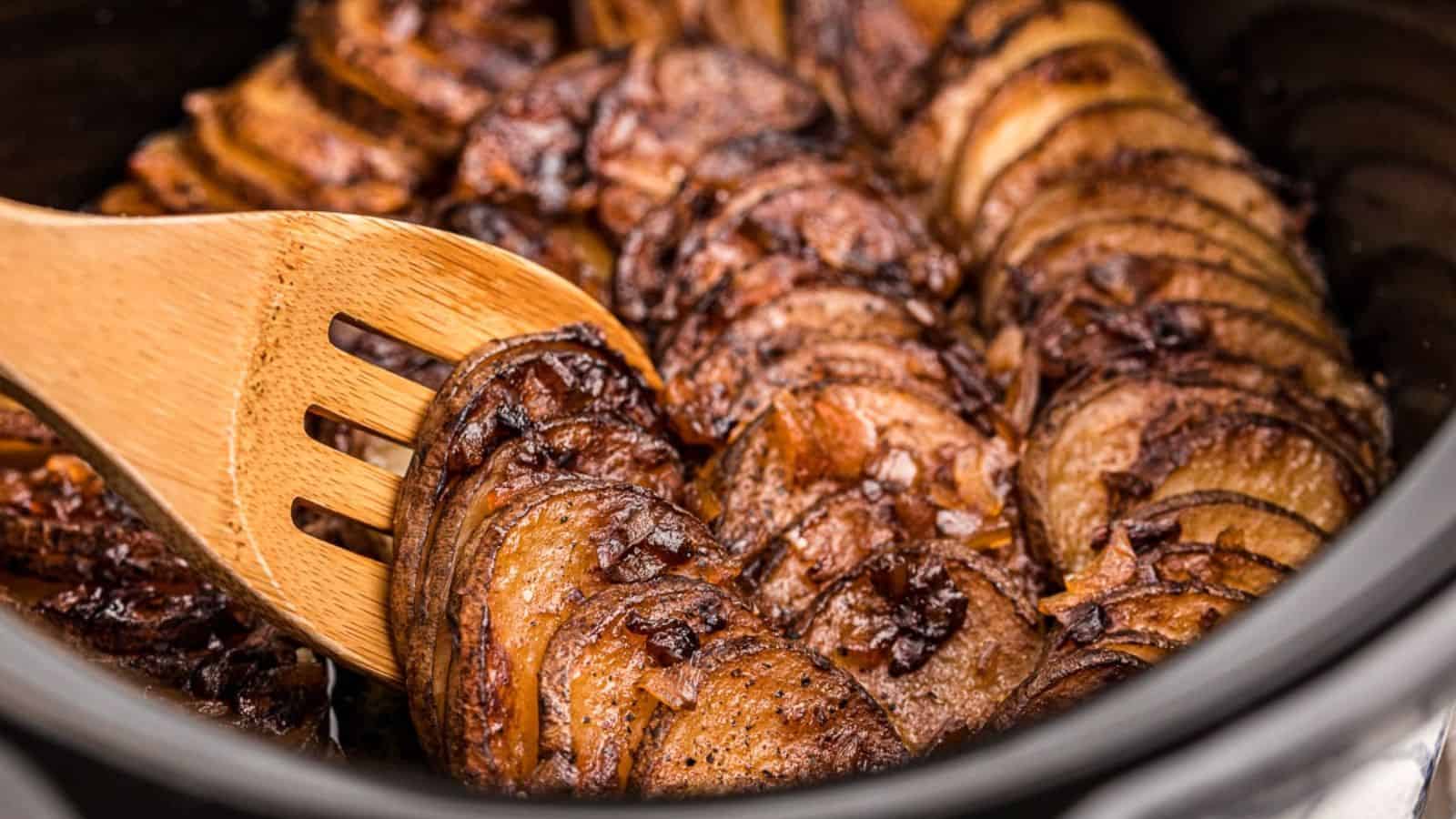 Sliced, caramelized onions in a slow cooker, with a wooden spatula gently lifting them, showcasing their rich, golden-brown color.