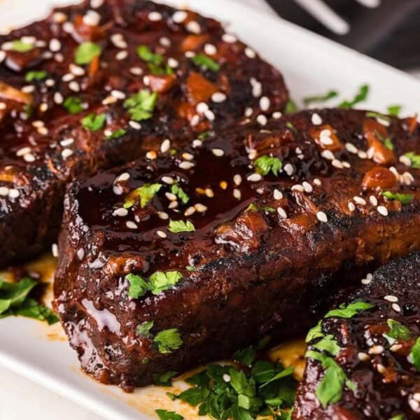 Three succulent, glazed meatloaf slices garnished with sesame seeds and fresh herbs on a white platter, showcasing rich flavor and texture.