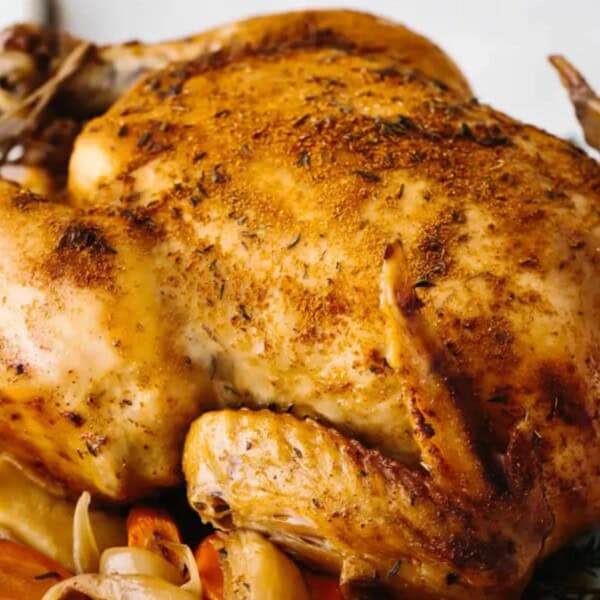 A beautifully roasted chicken on a platter, surrounded by vibrant carrots and herbs, showcasing a golden, crispy skin.