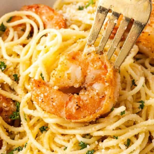 A fork lifts a shrimp from a bowl of spaghetti, garnished with parsley and sprinkled with cheese.
