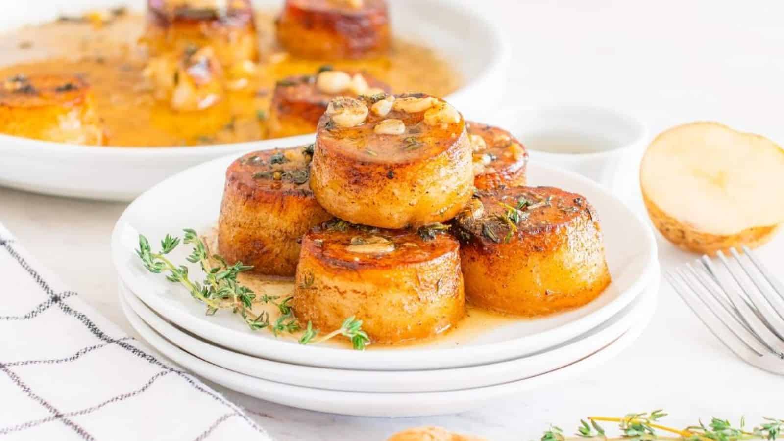Golden, caramelized potato rounds topped with herbs, served on a white plate with a sauce and fresh thyme, alongside a potato half.