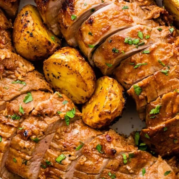 Sliced roasted meat with a golden-brown crust, garnished with herbs, served alongside crispy roasted potatoes.