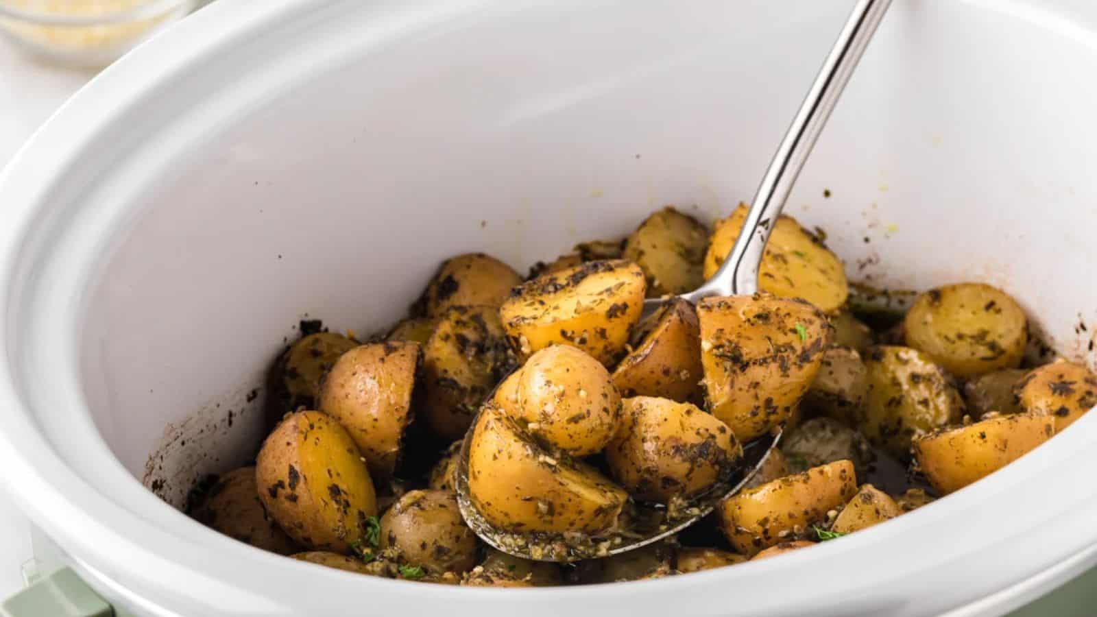 A close-up of seasoned, fork-tender baby potatoes in a slow cooker, mixed with herbs and spices, ready to be served.
