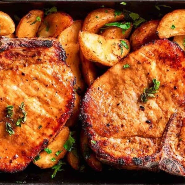 The image shows grilled pork chops garnished with herbs and roasted potato wedges in a baking dish.