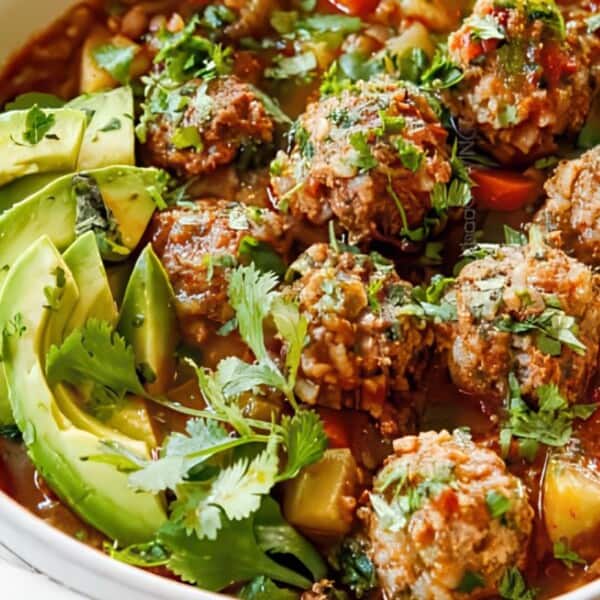 A bowl of flavorful Mexican meatball soup topped with sliced avocado and garnished with cilantro. The soup contains hearty meatballs with rice, vibrant vegetables, and a rich broth, creating a colorful and appetizing dish.