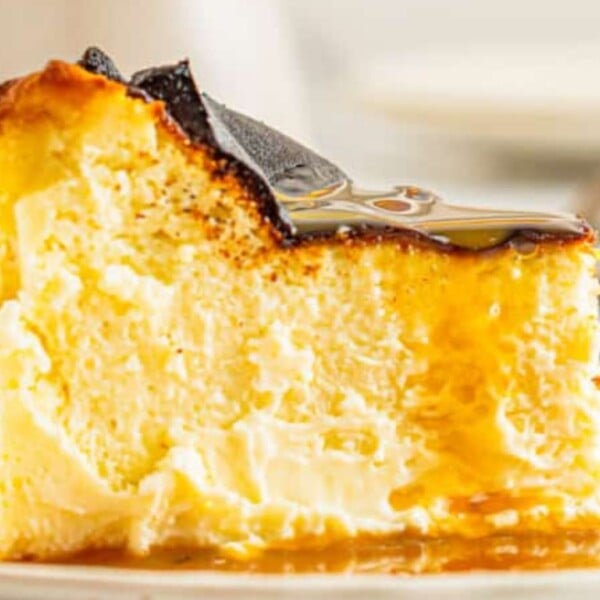 A slice of creamy cheesecake with a golden-brown caramelized topping, drizzled with syrup on a white plate.