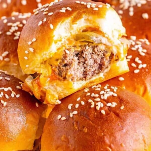 A close-up of golden-brown sliders with sesame seeds, showcasing a gooey cheese and juicy beef filling, surrounded by more sliders.
