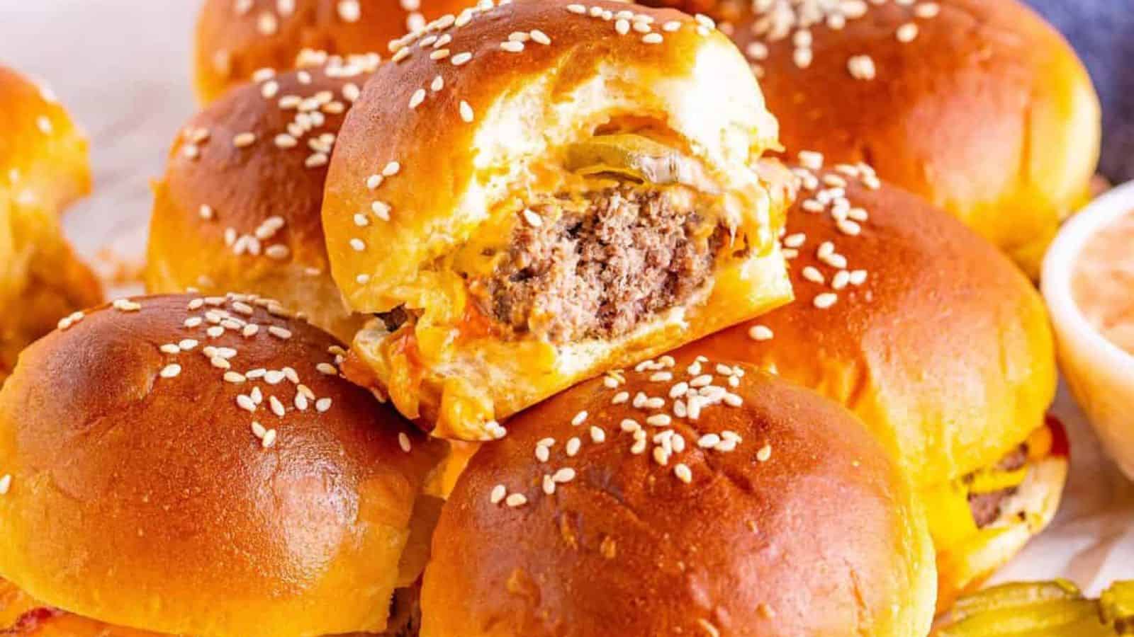 A close-up of golden-brown sliders with sesame seeds, showcasing a gooey cheese and juicy beef filling, surrounded by more sliders.